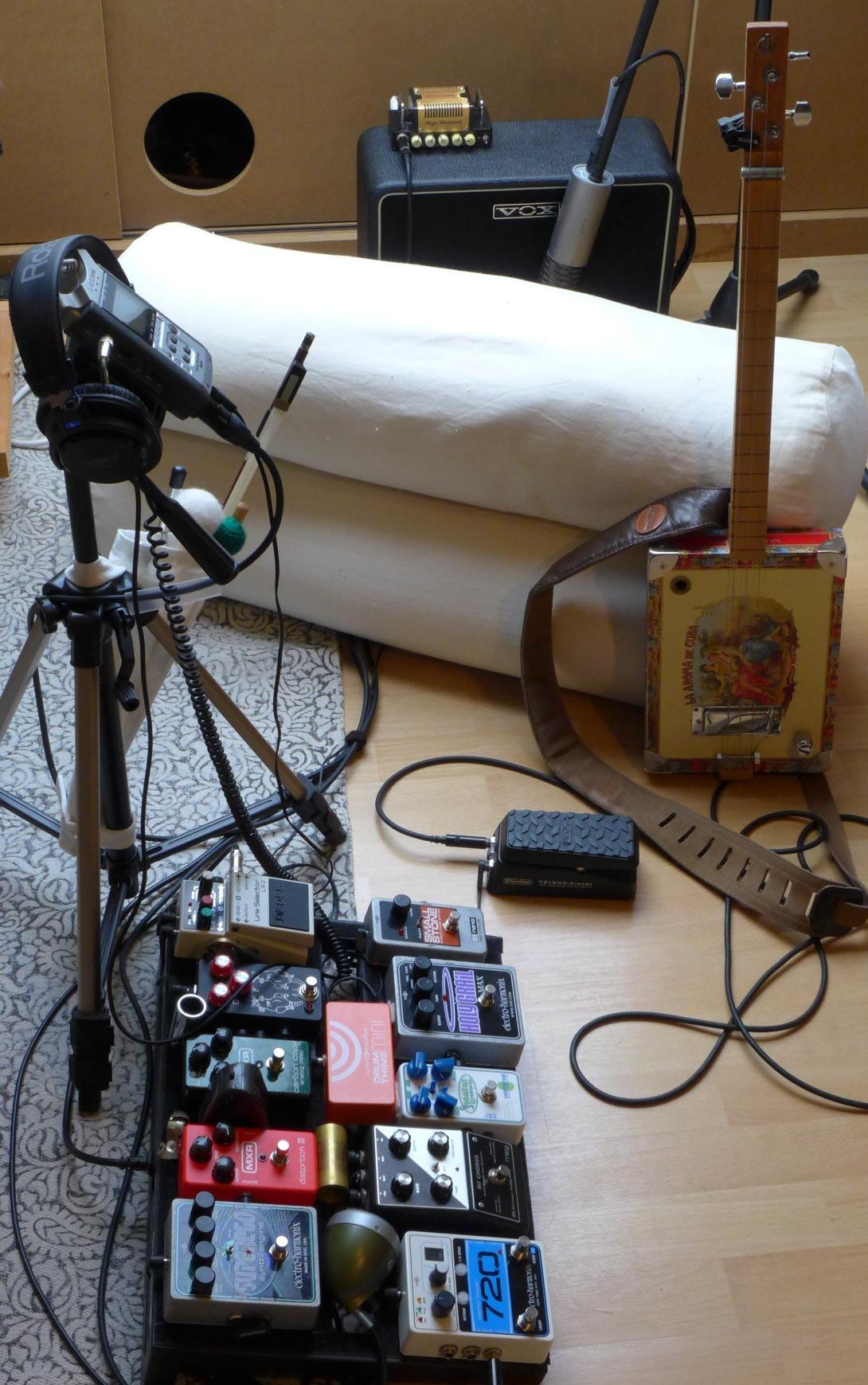 A photo of the studio showing a pedal board, a digital audio recorder,
                a cigar box guitar and an amplifier on the back